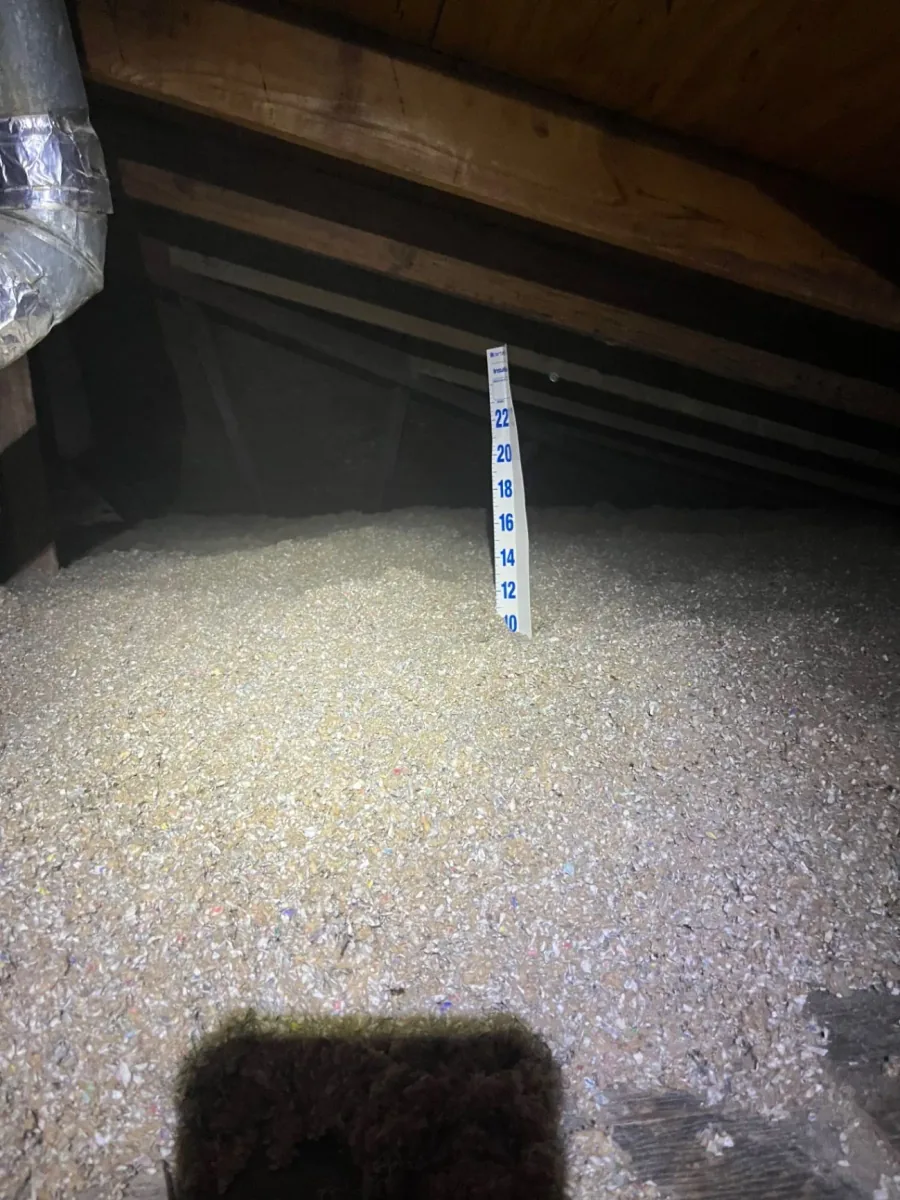 Close view of loose-fill cellulose insulation beneath attic rafters with a depth marker