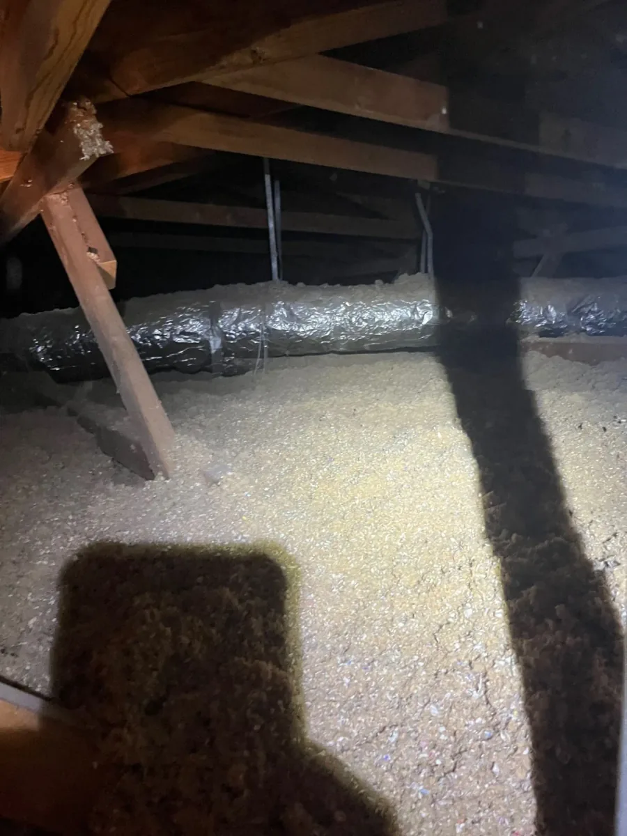 Loose-fill cellulose insulation across an attic floor beside reflective ductwork and wood framing