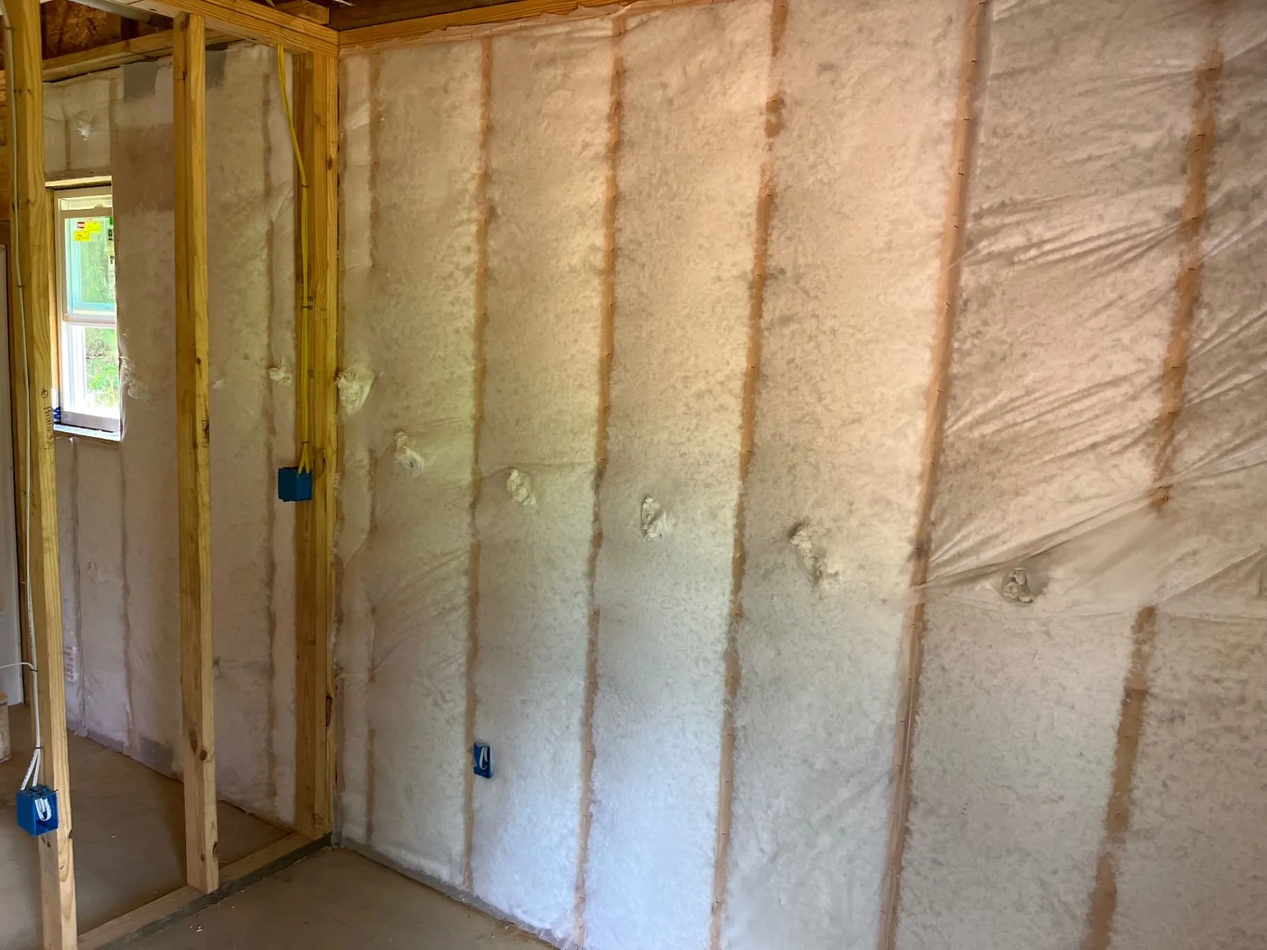 Close view of net-and-blow wall insulation filling open wall cavities around electrical boxes