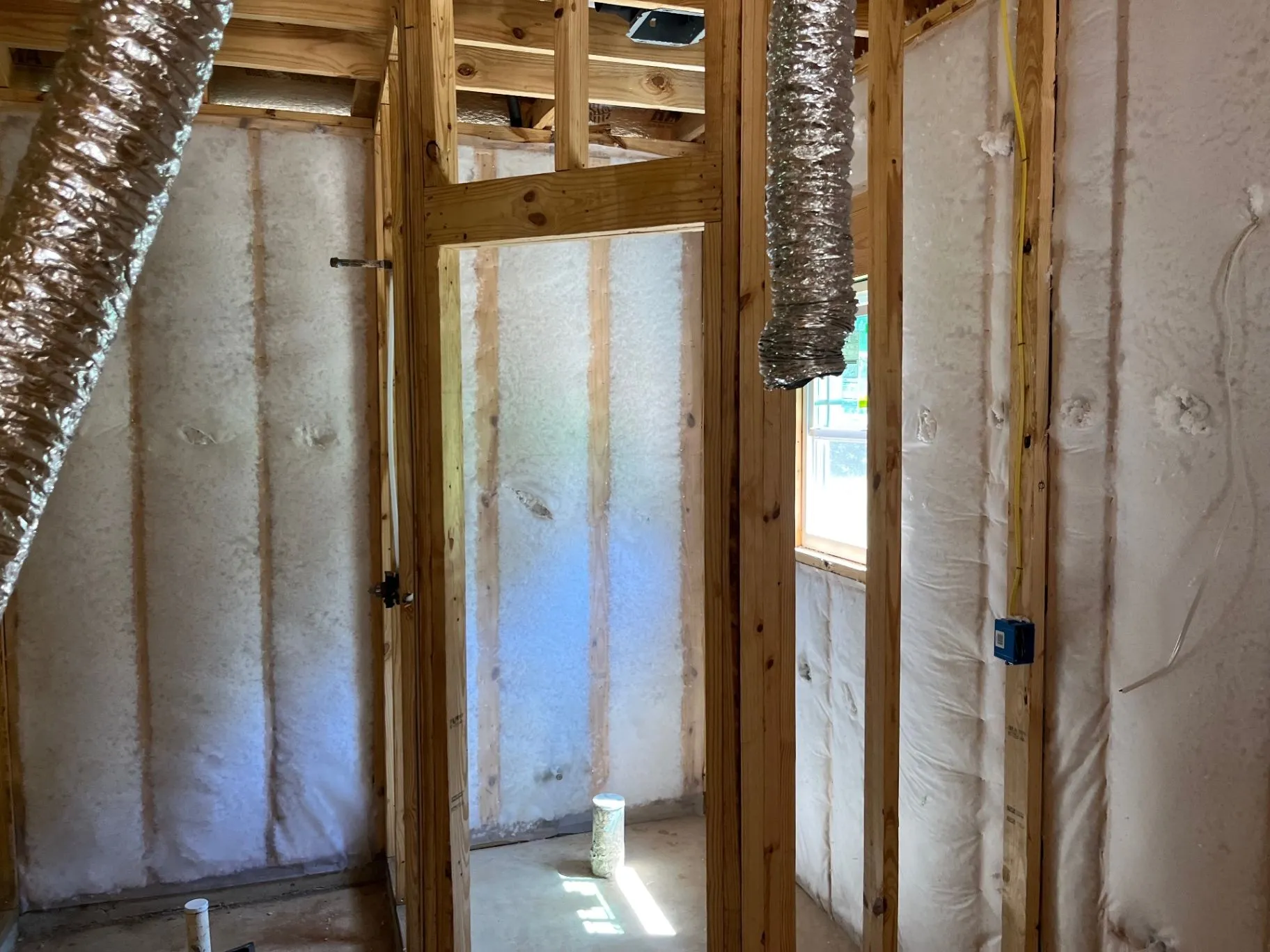 Net-and-blow wall insulation in open wall cavities beside exposed framing and a window