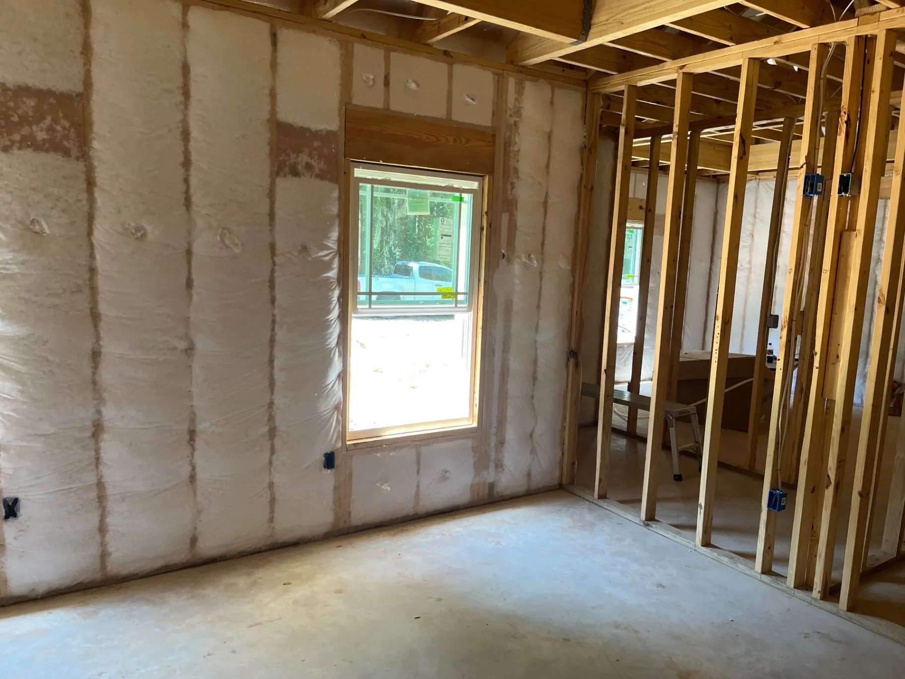 Open wood-framed room showing net-and-blow wall insulation around a window and adjoining wall